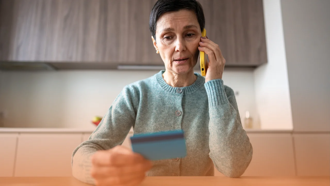 Znepokojená žena telefonuje a drží v ruke platobnú kartu počas podozrivého telefonátu.